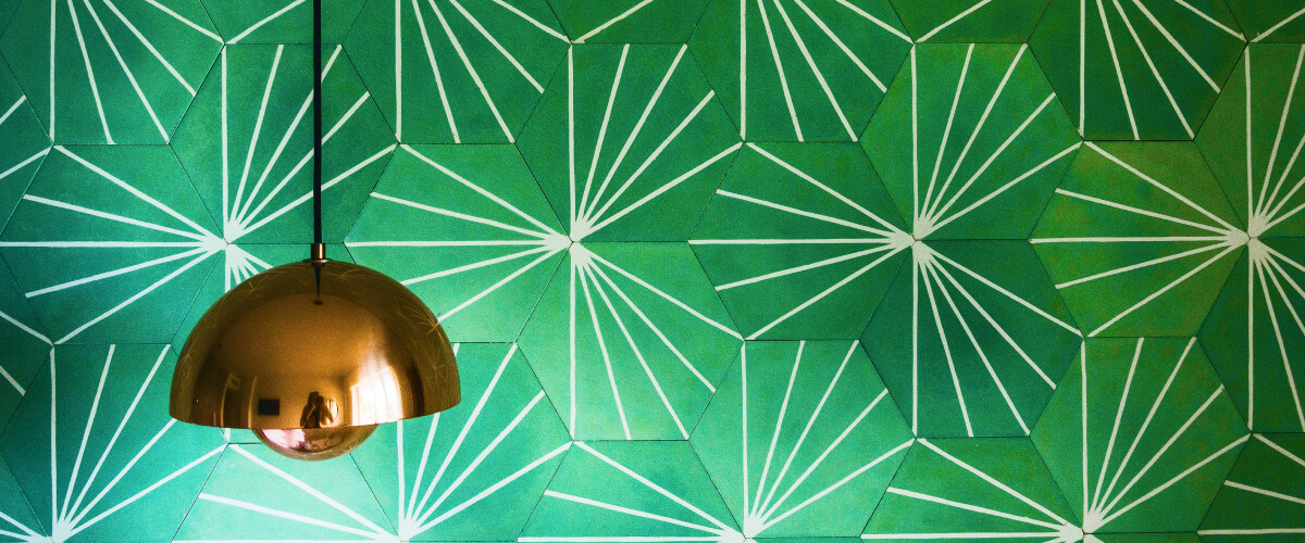 Taklampa som hänger med en grön vägg bakom på Designfynds "om oss sida"